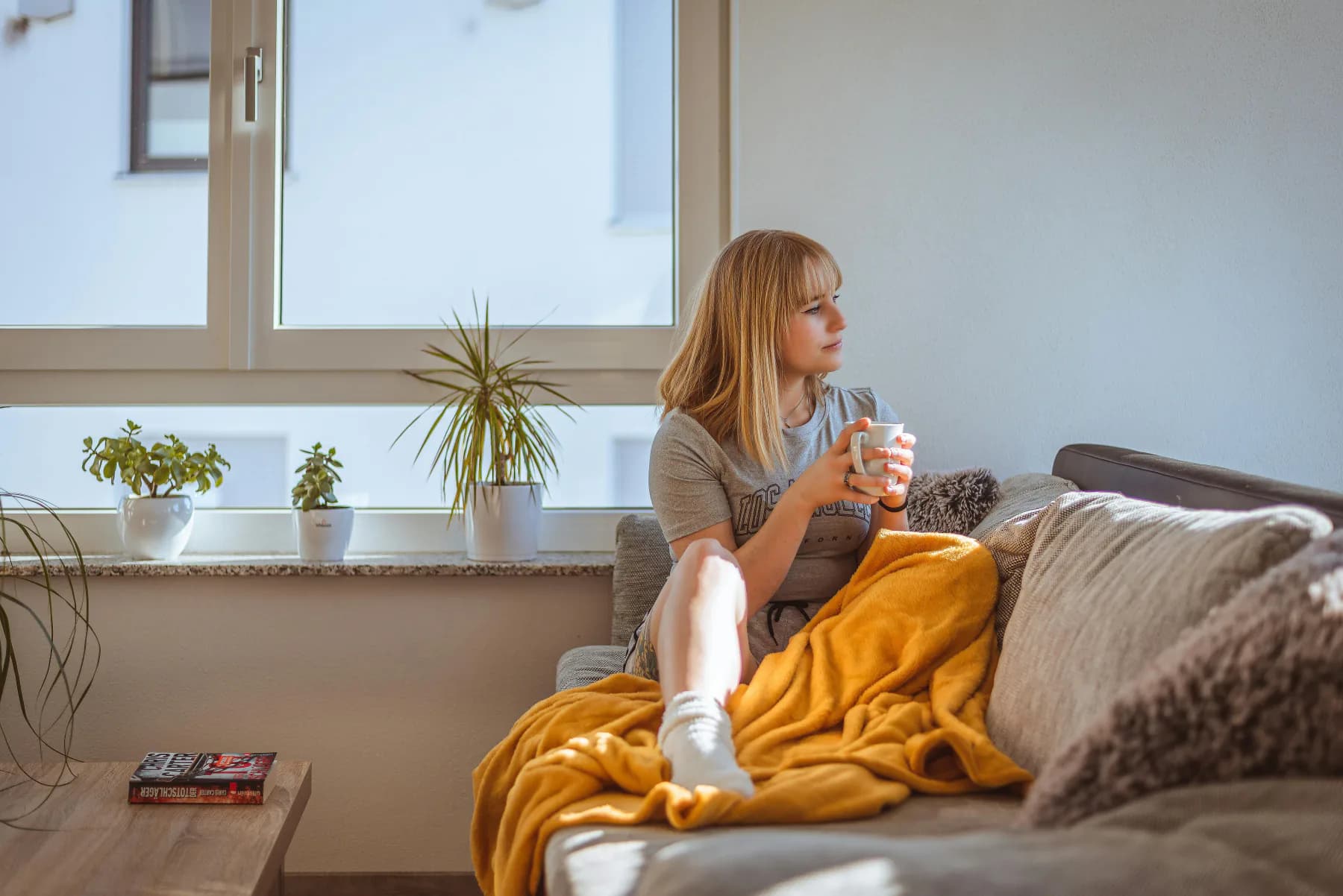 Ettertenksom person med kaffekopp ved vinduet hjemme